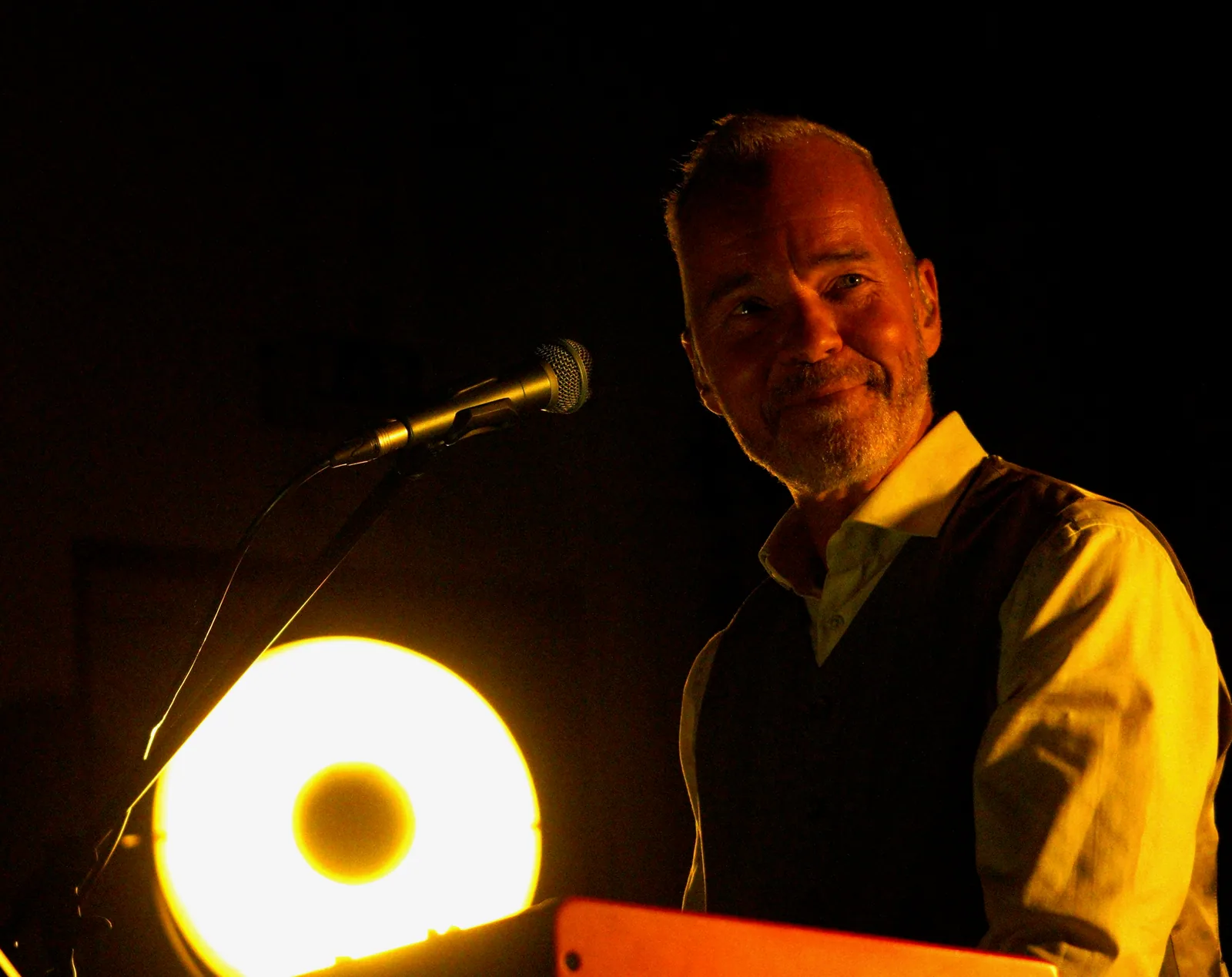 Henning Rietz am Mikrofon auf abgedunkelter Bühne, warm angeleuchtet