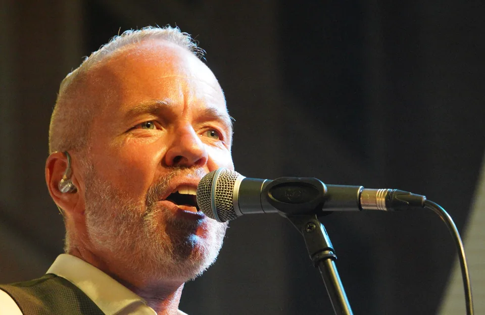 Henning Rietz beim Singen ins Mikrofon, In-Ear-Monitor, dunkler Bühnenhintergrund
